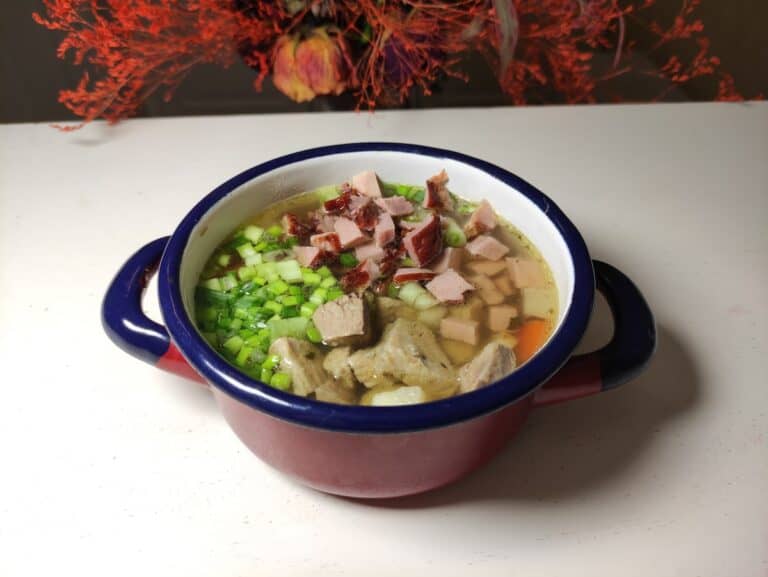 A bowl of Polish ham soup with meat and vegetables in it.