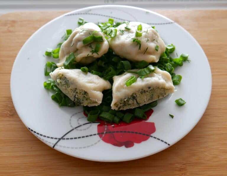 A plate with Polish spinach pierogi and green onions on it.