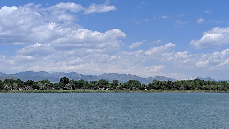 An image of a pristine blue lake with green trees, blue skies and mountains in the distance to celebrate World Water Day.