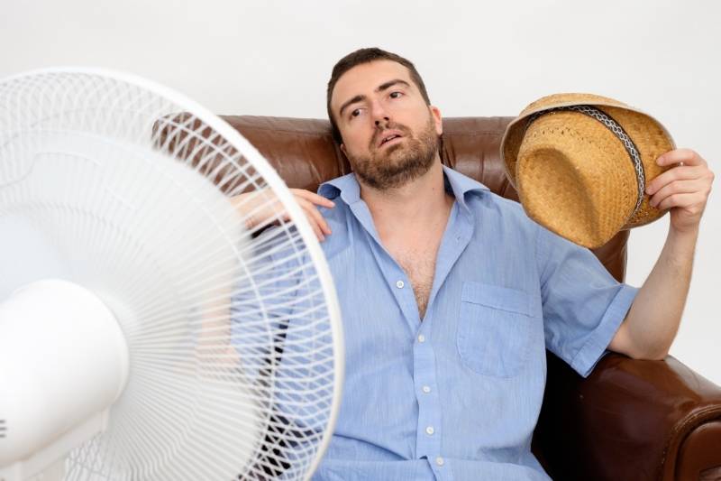 Flushed man feeling hot in front of a fan.