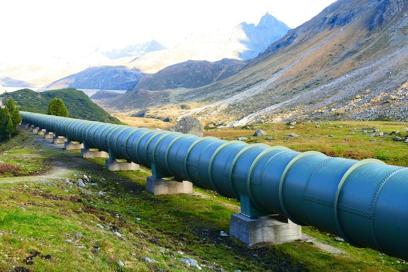 A large blue water pressure pipe runs through a mountain valley. This is water infrastructure. It's not invisible. It's right there.