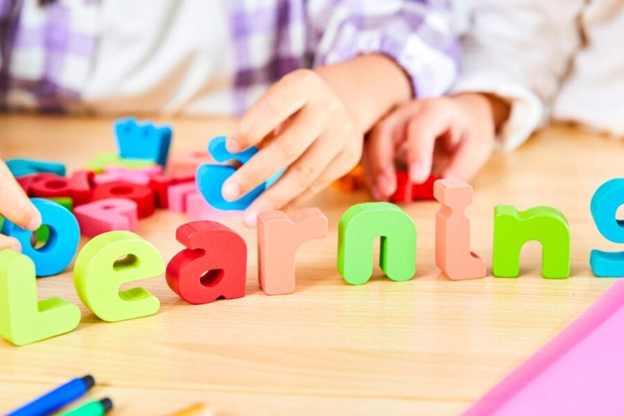 Children arranging colorful wooden letters spelling "learning" to illustrate the connection between ADHD and learning disabilities.
