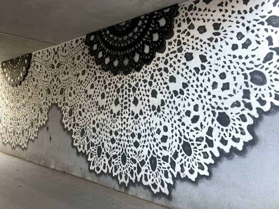 Large black and white lace doily patterns are painted on a concrete wall beneath an overpass, showcasing some of the best street art in Wroclaw.