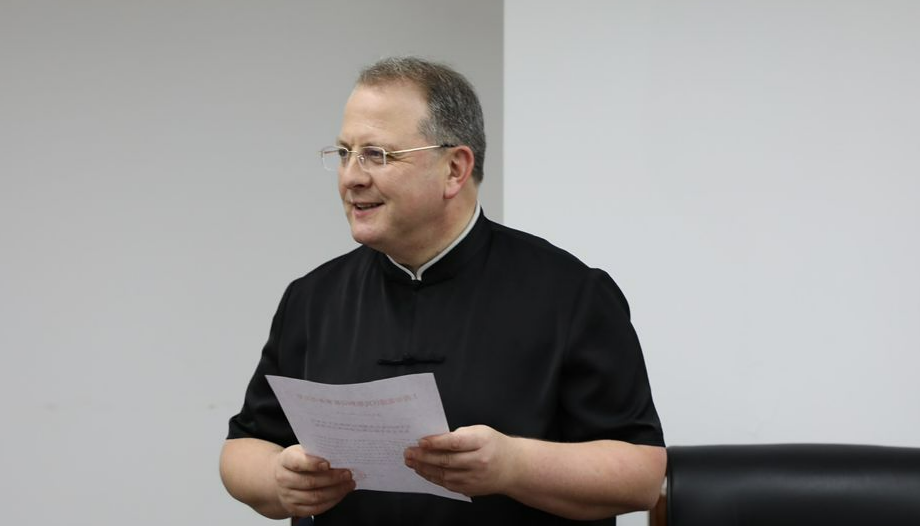 Un sacerdote sostiene unas hojas mientras parece explicar un asunto en un aula.