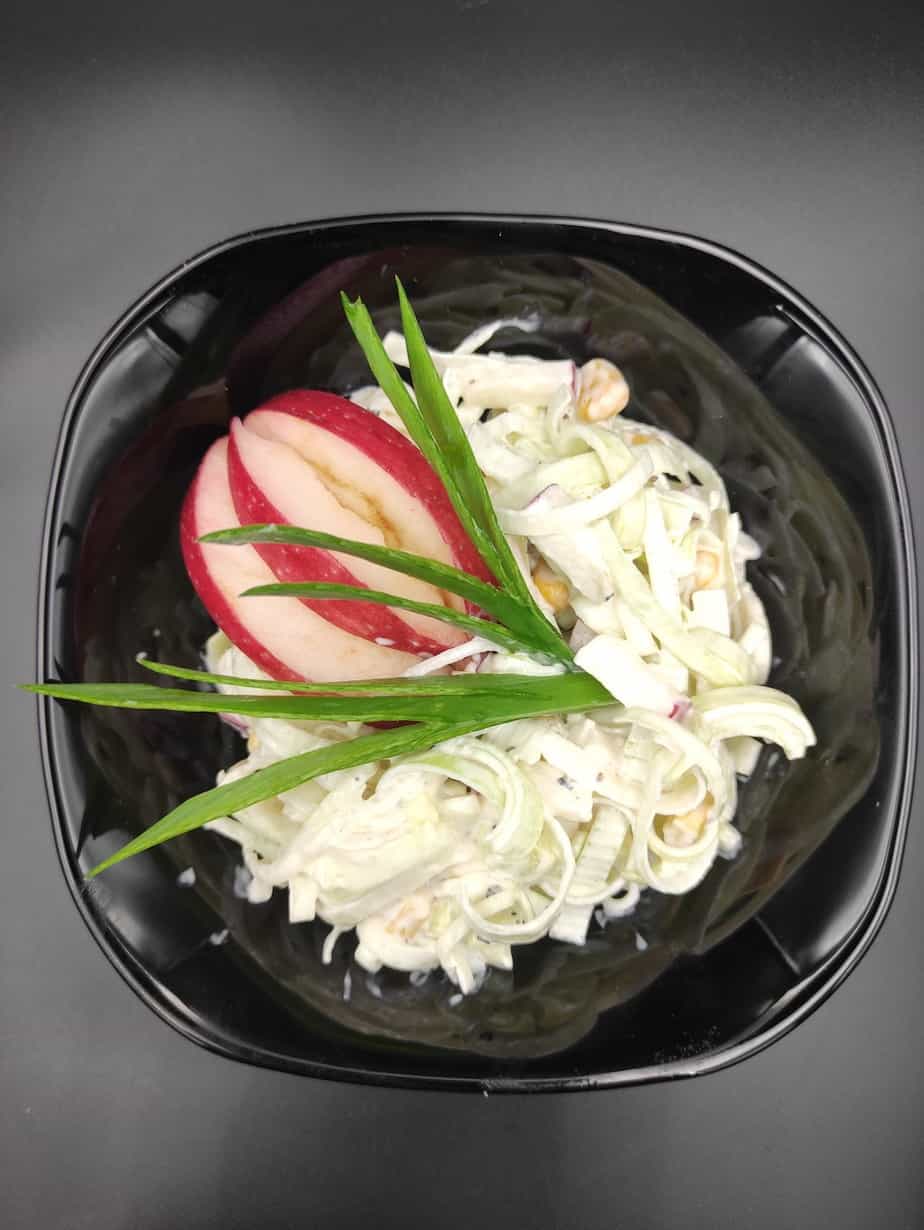 Polish leek salad garnished with apple slices in a black bowl.