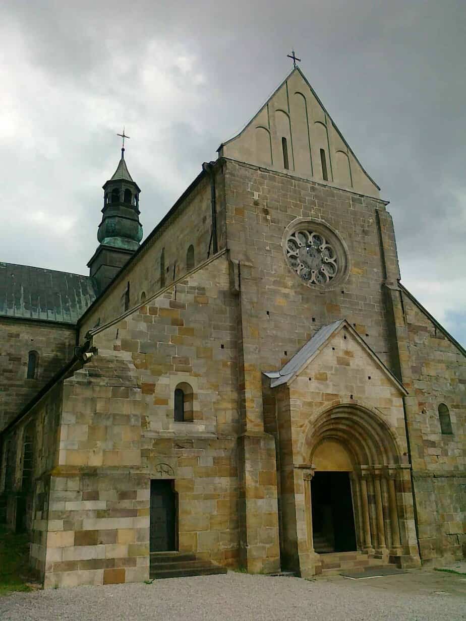 Stone Romanesque church with arched doorway, rose window, and a tall tower under a cloudy sky&mdash;one of the best places near Ł&oacute;dź to admire historic architecture in the Ł&oacute;dź Voivodeship.
