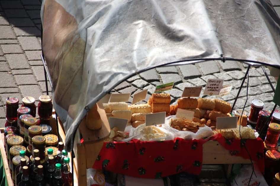 A market stall displays various breads, jars of preserves, and bottles under a canopy, with handwritten labels on the items&mdash;perfect for discovering unique Poland souvenirs or finding things to buy in Poland.