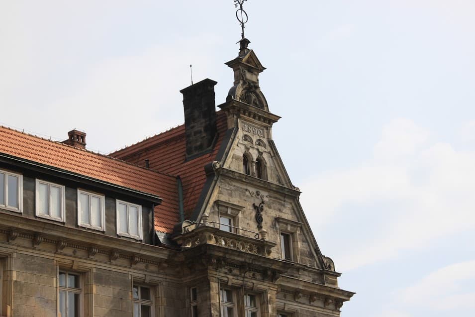 Historic stone building with a red-tiled roof, arched windows, and an ornate triangular pediment featuring a decorative clock and weather vane&mdash;just steps from some of the Best Street Art in Wroclaw.
