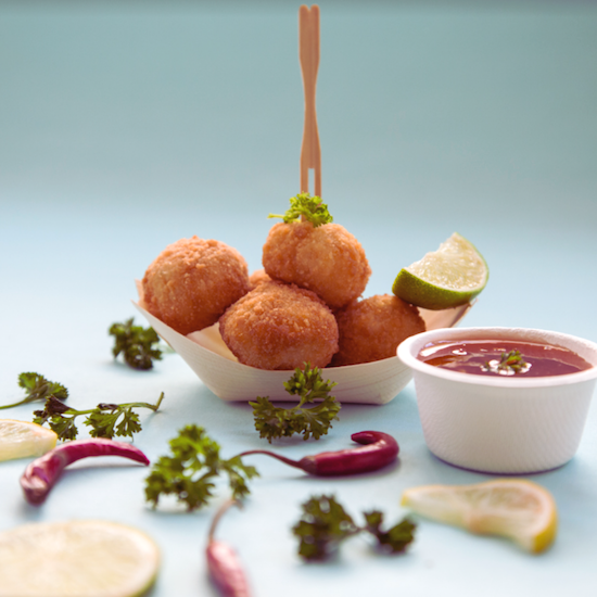 A wooden boat holding balls with a bamboo fork and a sugarcane taster bowl holding sauce