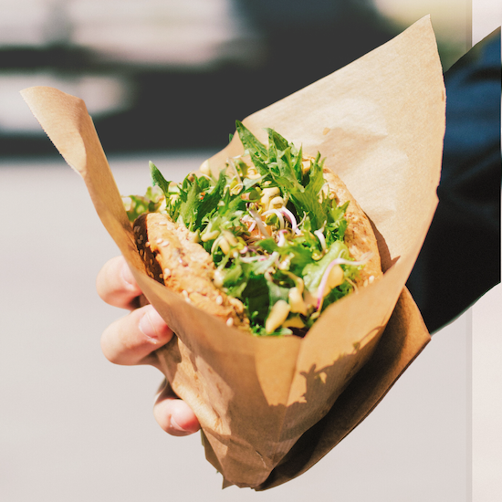 A hand holding a salad filled bread roll wrapped in greaseproof paper