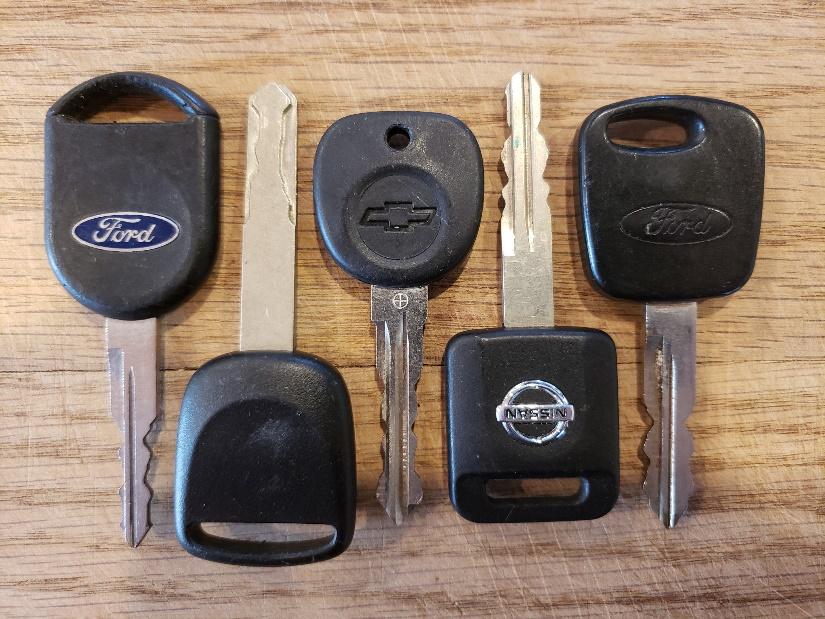 A set of five car keys from Ford, Chevrolet, and Nissan, displayed on a wooden surface.