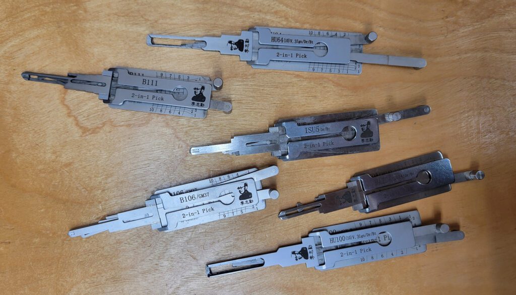 A set of six Lishi 2-in-1 lock pick tools arranged on a wooden surface.