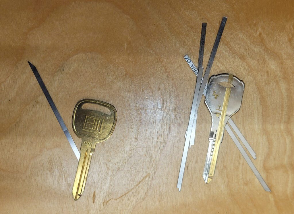 Two keys on a wooden surface, each accompanied by several thin decoder strips used for lock reading."