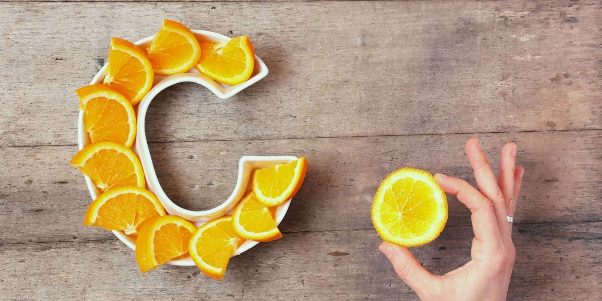 A hand is about to pick up a slice from a ceramic plate shaped like a C, which is artistically arranged with orange slices on a wooden surface in Idaho.