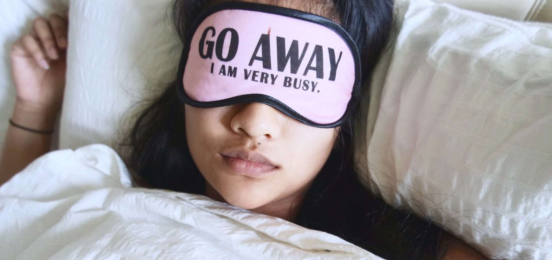 A person resting in bed in Meridian, Idaho, with a sleep mask that reads "go away I am very busy.