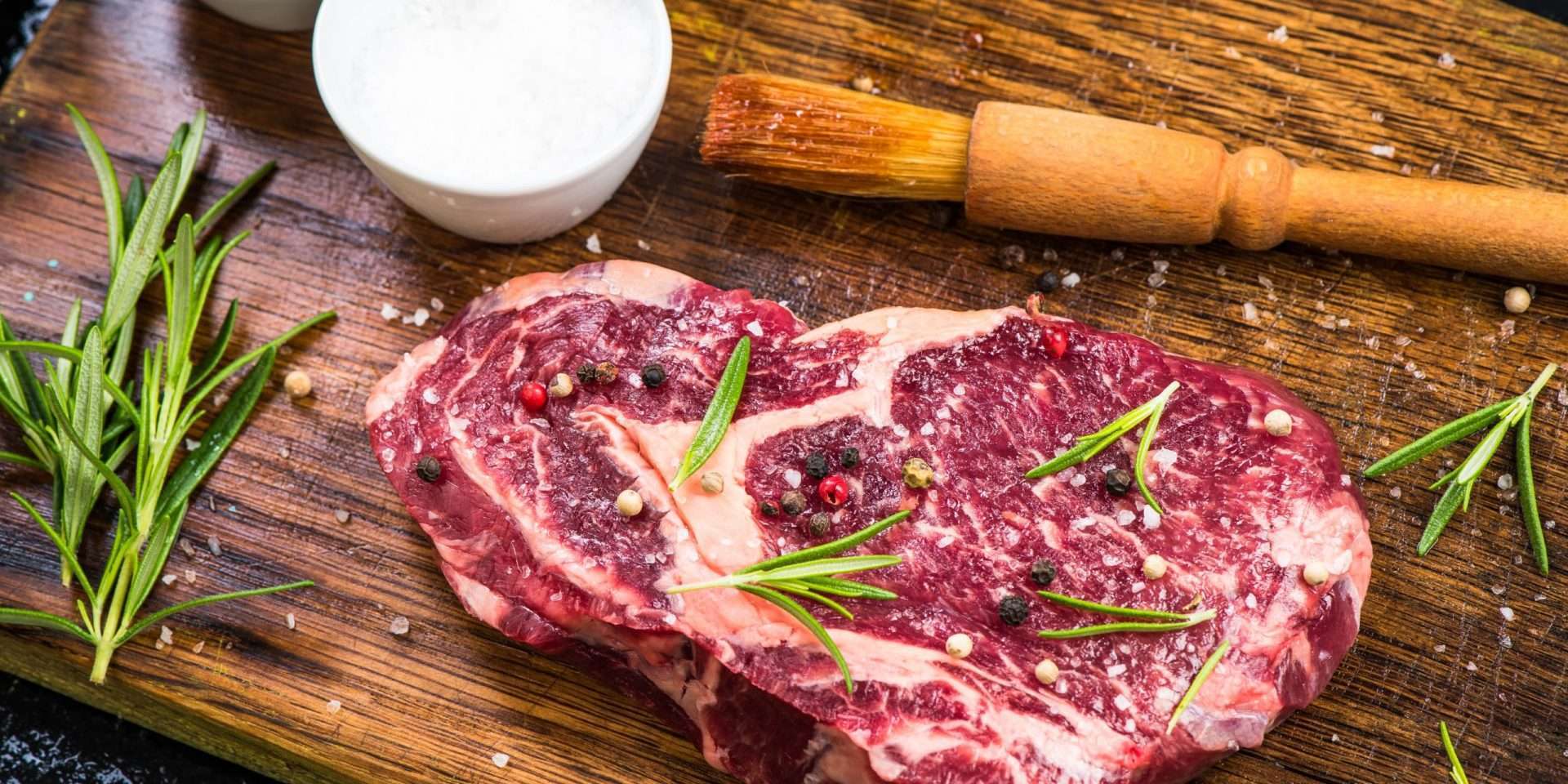 Raw steak in the shape of a heart seasoned with peppercorns and herbs on a wooden cutting board, celebrated by functional medicine enthusiasts in Boise.