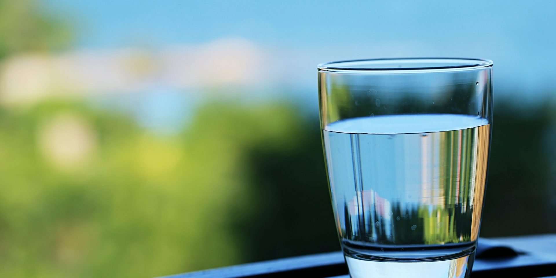 A clear glass of water on a railing with a blurred naturopathic medicine background.