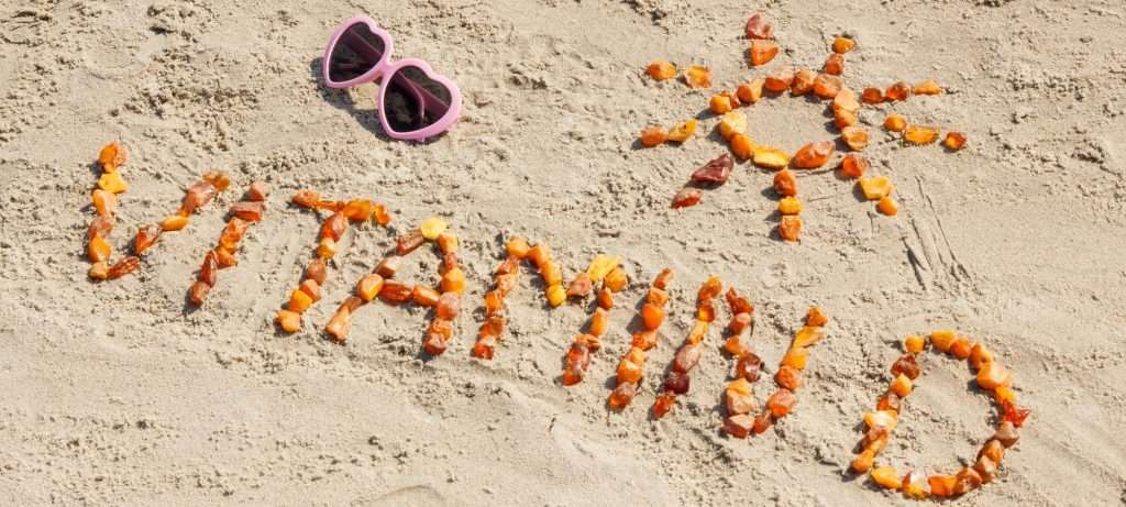 Sunglasses, inscription vitamin D and shape of sun on sand at beach