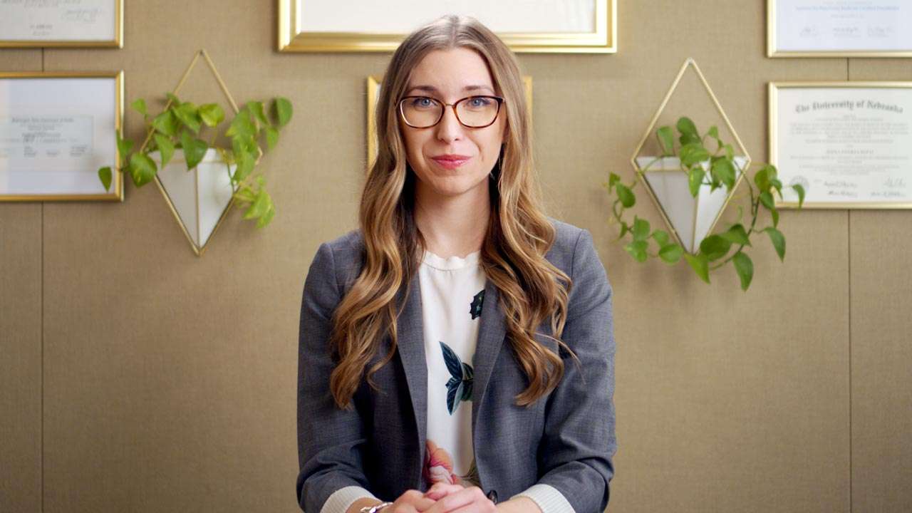 Dr. Alexa NMD sitting in an office environment in Boise, Idaho, framed by diplomas in functional medicine and a plant in the background.