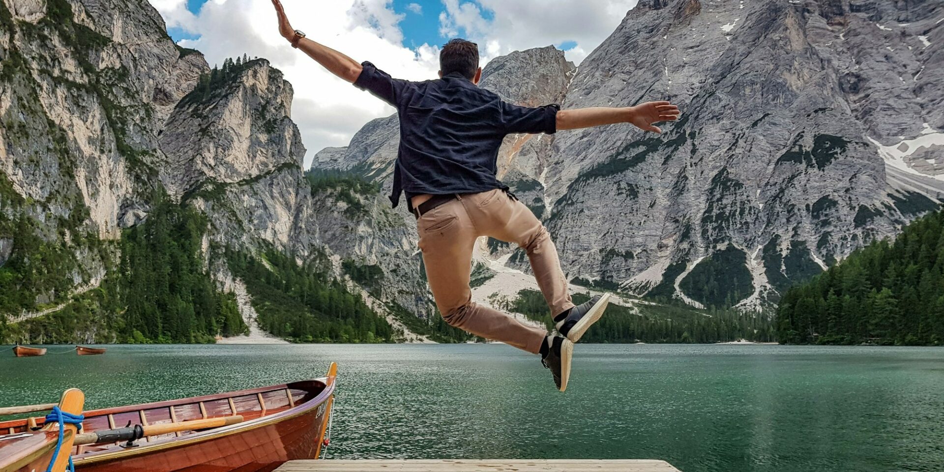 Rear view of man jumping on wooden deck by lake. Happy person in idyllic place in nature.