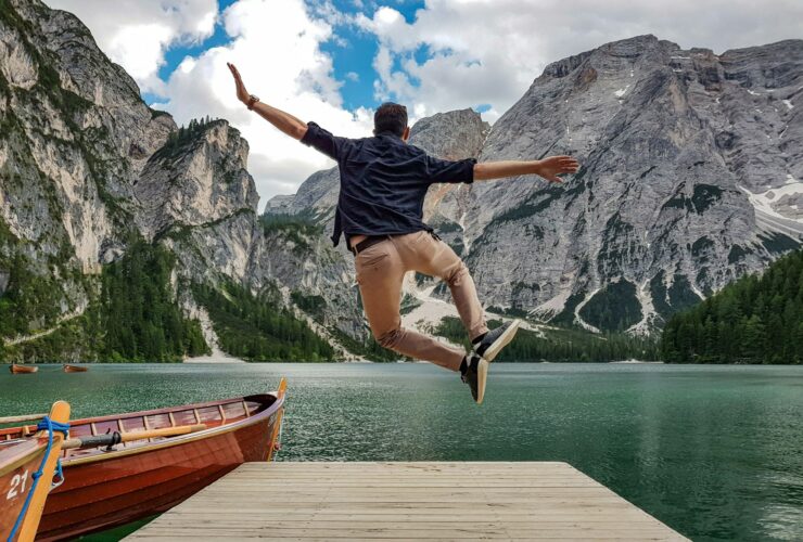 Rear view of man jumping on wooden deck by lake. Happy person in idyllic place in nature.