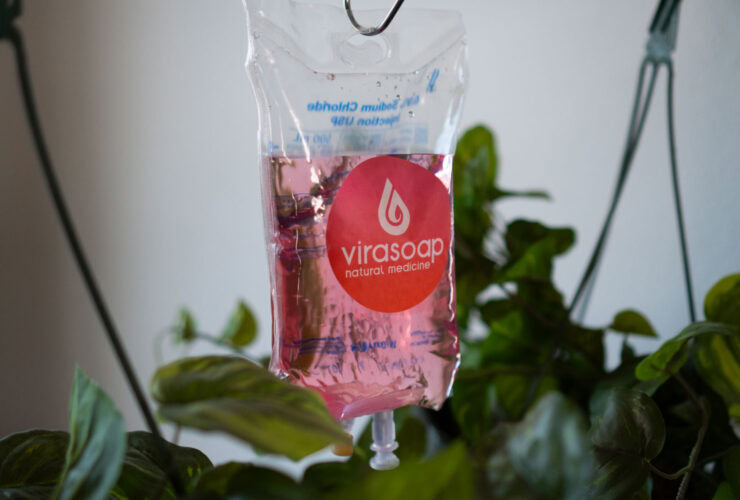 A pink liquid-filled Virasoap pouch hangs among green leaves, showcasing its bold branding on the front. Discover the dynamic benefits of NAC infused within, promising a rejuvenating experience with every use.