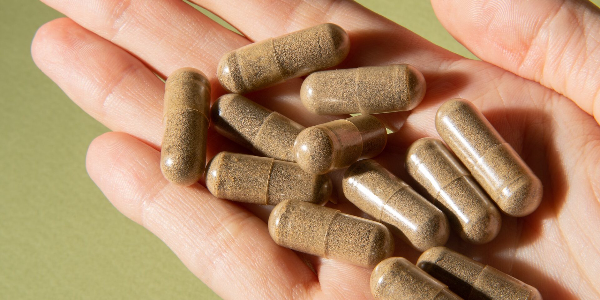 Natural herbal tablets in capsules in a hand on a light green background.
