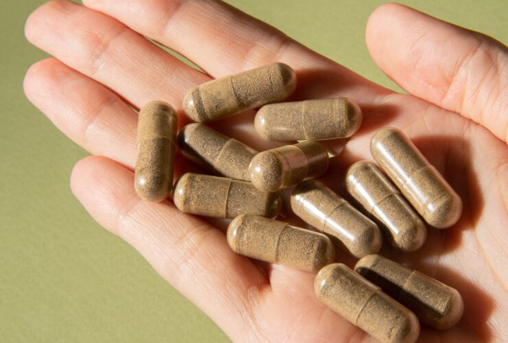 Natural herbal tablets in capsules in a hand on a light green background.