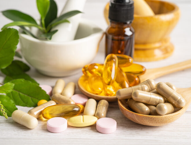 Assorted capsules, softgels, and tablets arranged with fresh herbs, a mortar and pestle, and a small brown dropper bottle on a light wooden surface highlight the importance of supplement safety when considering Amazon supplements.