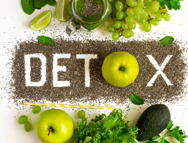 The word "Detox" is spelled with chia seeds on a white surface, surrounded by green apples, grapes, lettuce, avocado, lime, and a green smoothie—perfect inspiration to detoxify your life and age well naturally.