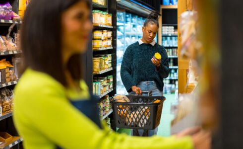 Woman choosing healthy food in organic supermarket reading a label holding shopping basket