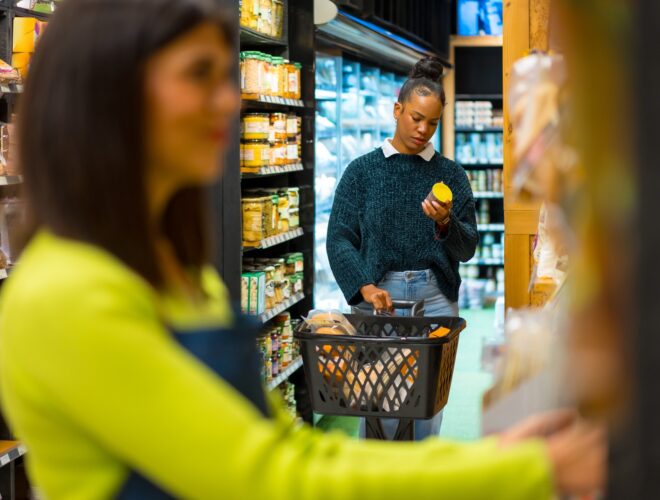 Woman choosing healthy food in organic supermarket reading a label holding shopping basket