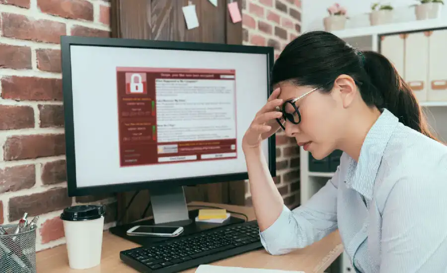 Concerned individual at a computer workstation with a security warning on the screen, indicative of a cybersecurity issue, data breach, or critical error requiring urgent attention.