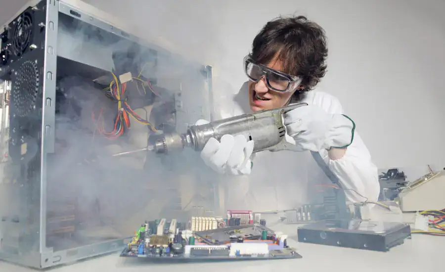 Person in lab coat humorously using an oversized power drill on an open computer case, suggesting a comical take on hardware repair or maintenance.