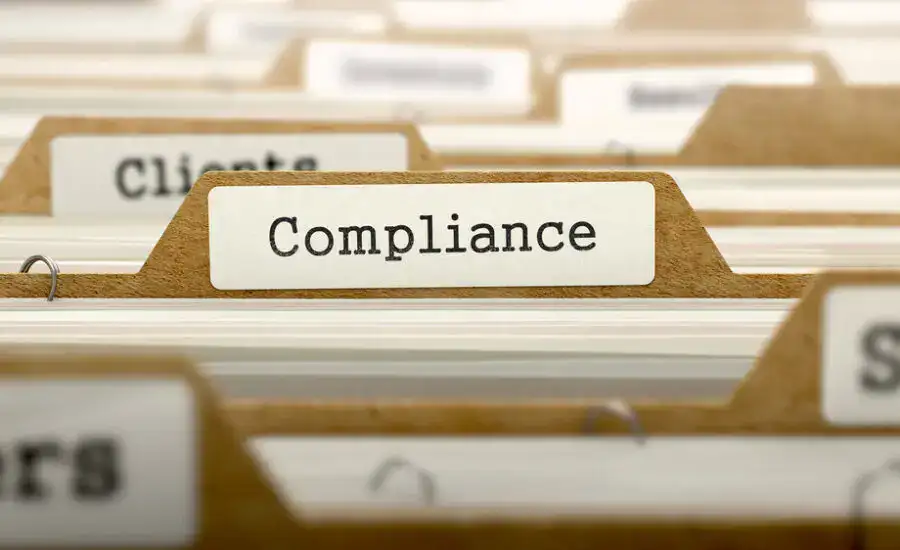 Focused view on a file tab marked 'Compliance' among other categorized tabs in a filing cabinet, representing organization and adherence to laws and regulations in a business setting.