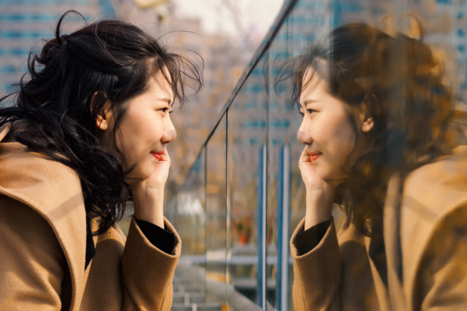 Beautiful Chinese girl looking at her mirror image in glass. Mirror and shadow reference for accent reduction.