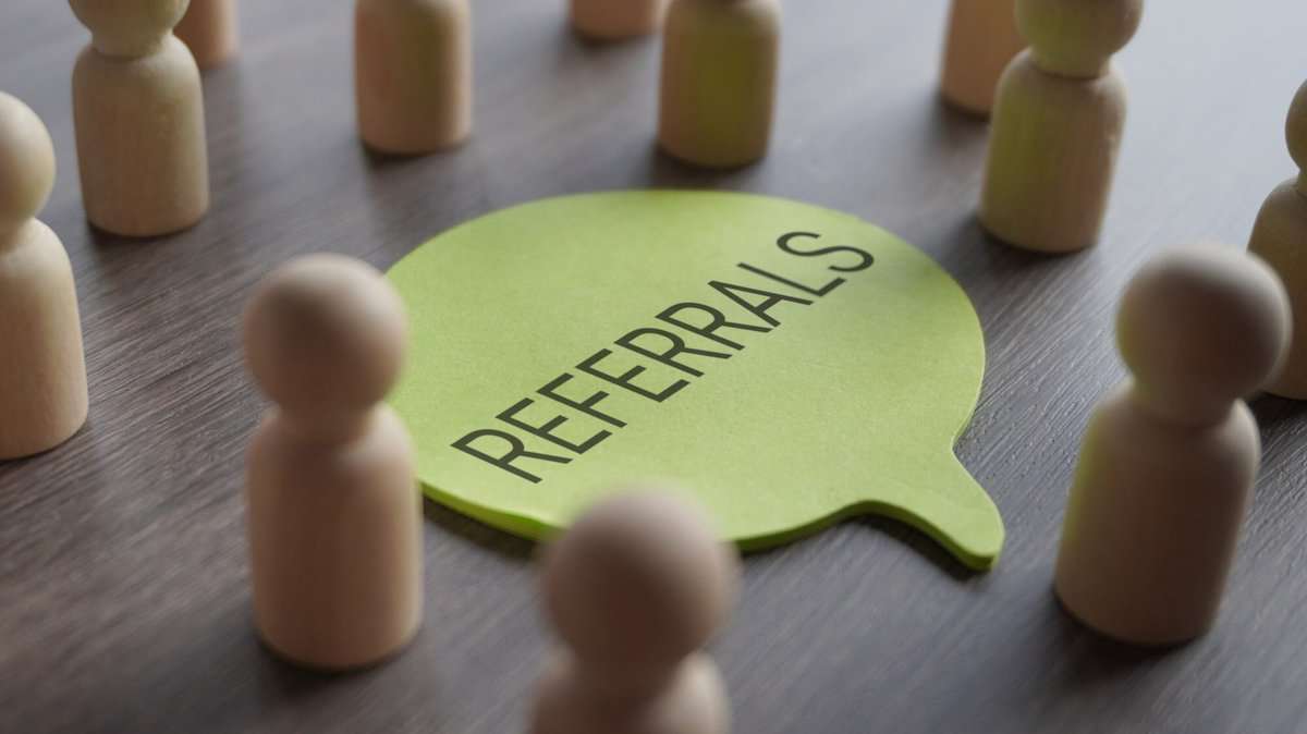 A group of wooden figurines surrounding a speech bubble with text REFERRALS.