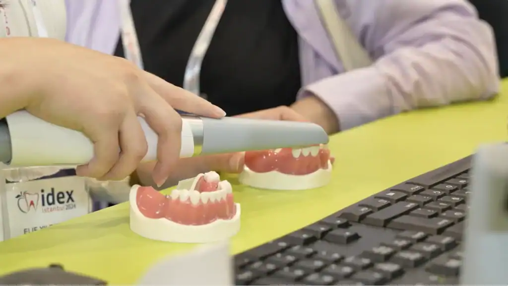 Dentium İFM Etkinliği Video Çekimi | Kongre ve Kurumsal Etkinlik Prodüksiyonu-3 - Pippet Creative - Pippet Creative Hands hold a handheld intraoral scanner over dental models on a bright lime counter, with a keyboard nearby