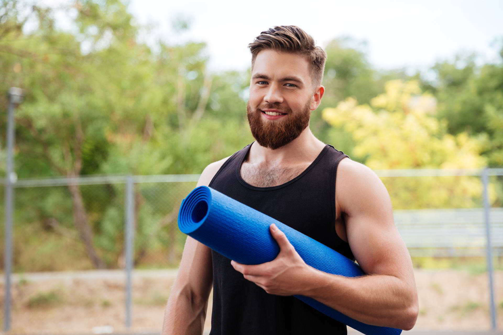 handsome bearded young sportsman holding yoga looking camera outdoors